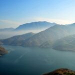Serene mountain lake with mist and winding roads, perfect for nature and travel themes.