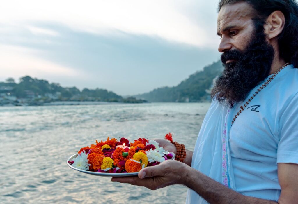 Man performing traditional ritual with flowers on the Ganges River in Rishikesh, India.