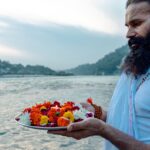 Man performing traditional ritual with flowers on the Ganges River in Rishikesh, India.